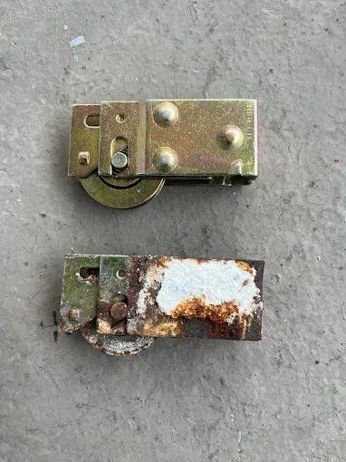 Old rusted sliding door roller assembly beside a new roller assembly